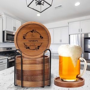 May include: A set of wooden coasters with a black metal holder. The top coaster is engraved with "the SIMON family" within a decorative wreath. A glass mug of beer sits on a matching coaster.