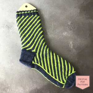 Op de afbeelding: Een gestreepte gebreide sok in groen en donkerblauw met een hiel en teen. De sok hangt aan een houten label met de tekst "DIGITAL PDF PATTERN".