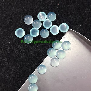 May include: A collection of pale blue cabochon gemstones, some on a silver tray and some scattered on a black surface.