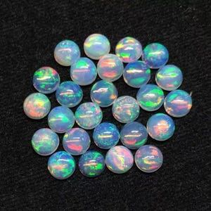 Puede incluir: Una colección de 20 cabujones de ópalo iridiscente, cada uno con un patrón único de color y brillo. Los cabujones son redondos y tienen una superficie lisa y pulida.
