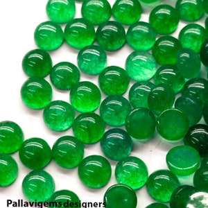 Op de afbeelding: Een verzameling ronde, groene cabochon edelstenen. De stenen zijn glad en gepolijst, met een lichte translucentie. Ze zijn verspreid over een wit oppervlak.