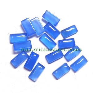 Puede incluir: Un conjunto de gemas rectangulares de color azul claro, pulidas y brillantes. El texto "PALLAVIGEMSDESIGNERS" es visible en verde. Estas gemas son probablemente para la fabricación de joyas o artesanía.