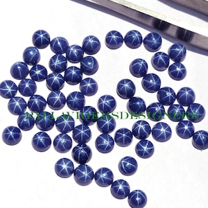 Puede incluir: Una colección de 30 cabujones redondos de zafiro estrella azul. Los cabujones tienen aproximadamente 4 mm de diámetro y presentan un patrón en forma de estrella.