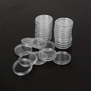 May include: Clear plastic coin holders, stacked and scattered, against a dark background. The holders are round with a clear, transparent design, suitable for protecting and displaying coins. The image shows multiple stacks and individual holders.