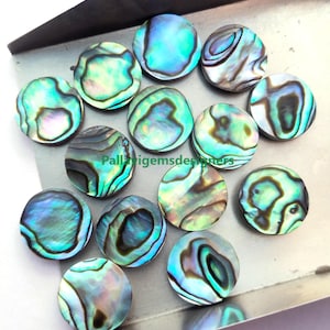May include: Assortment of 13 round iridescent abalone shell cabochons in various shades of green, blue, and purple. The cabochons are smooth and polished, with a natural, organic pattern.