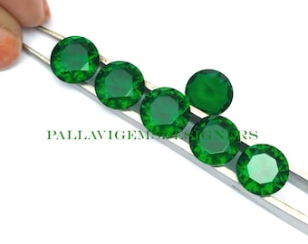 May include: Seven round, faceted, green gemstones on a silver tweezers. The gemstones are approximately 1 cm in diameter.
