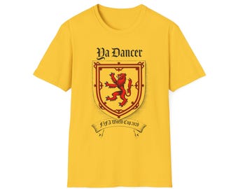 Puede incluir: Camiseta amarilla mostaza con un diseño de escudo heráldico. El escudo presenta un león rojo rampante. El texto "Ya Dancer" está arriba y "FIFA World Cup 2026" abajo.