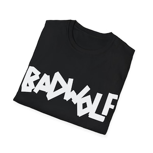 Peut inclure: Un t-shirt noir à manches courtes avec le texte BADWOLF imprimé en grandes lettres capitales blanches et grasses sur la poitrine. Le vêtement est plié, révélant un col rond et un design épuré avec une typographie à fort contraste.