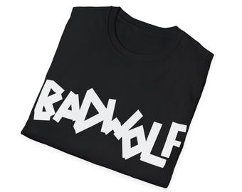 May include: A black short-sleeved t-shirt featuring the text BADWOLF printed in large, bold, white capital letters across the chest. The shirt is folded, displaying a crew neckline and a clean, minimalist design with high-contrast typography.
