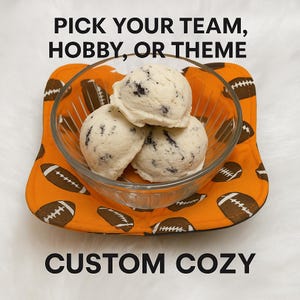 Puede incluir: Un cuenco de vidrio con tres bolas de helado de galletas y crema, sobre un posavasos naranja con estampado de f&uacute;tbol. El posavasos tiene balones de f&uacute;tbol marrones. El texto de la imagen dice "PICK YOUR TEAM, HOBBY, OR THEME" y "CUSTOM COZY."