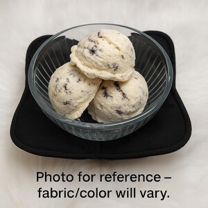 Puede incluir: Tres bolas de helado de galletas y crema en un cuenco de cristal transparente, sobre un salvamanteles cuadrado negro. El helado es blanco con trozos de galleta de chocolate negro. El texto en la parte inferior dice "Foto de referencia - la tela/el color pueden variar."