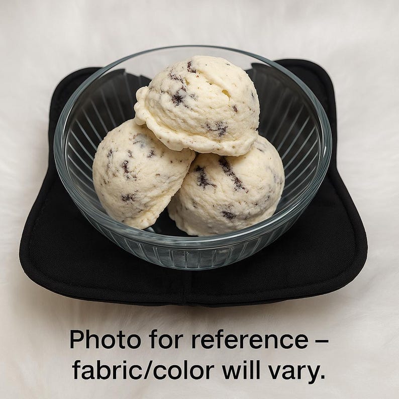 Puede incluir: Tres bolas de helado de galletas y crema en un cuenco de cristal transparente, sobre un salvamanteles cuadrado negro. El helado es blanco con trozos de galleta de chocolate negro. El texto en la parte inferior dice "Foto de referencia - la tela/el color pueden variar."