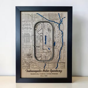 May include: A framed wooden map of the Indianapolis Motor Speedway featuring a layered design with natural wood tones and blue accents. The artwork displays the track layout, surrounding roads, and the text Indianapolis Motor Speedway, Speedway, Indiana, United States, Since 1909.