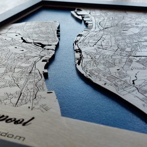 Pu&ograve; includere: Una mappa di legno di Liverpool, Regno Unito, con sfondo blu. La mappa &egrave; in rilievo e mostra le strade e le vie d'acqua della citt&agrave;.