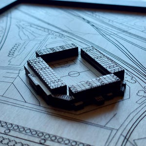 Pu&ograve; includere: Un modello in legno di uno stadio con un design dettagliato, posto su uno sfondo simile a una mappa. Lo stadio &egrave; in legno scuro e presenta un motivo a griglia all'esterno.
