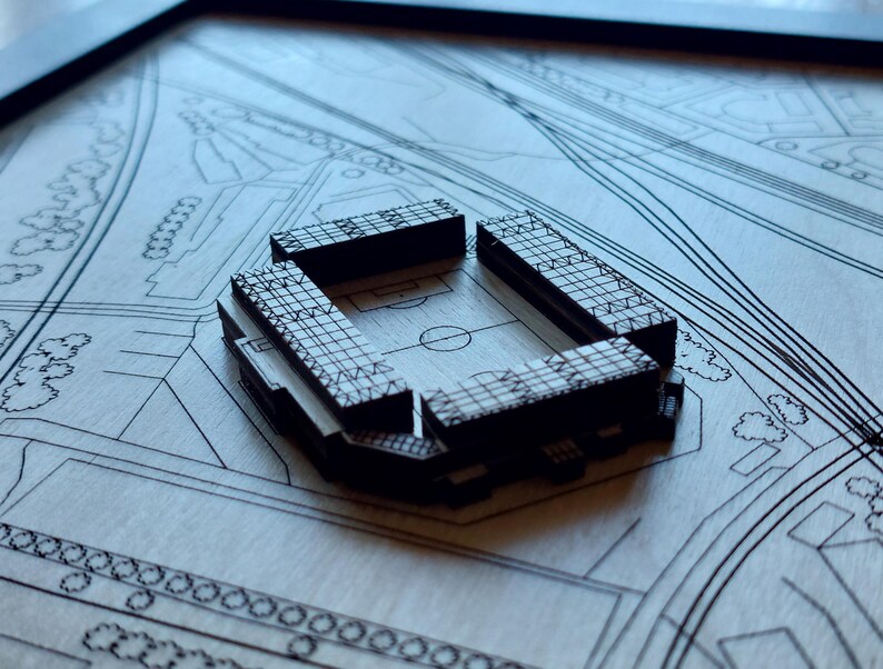 Pu&ograve; includere: Un modello in legno di uno stadio con un design dettagliato, posto su uno sfondo simile a una mappa. Lo stadio &egrave; in legno scuro e presenta un motivo a griglia all'esterno.