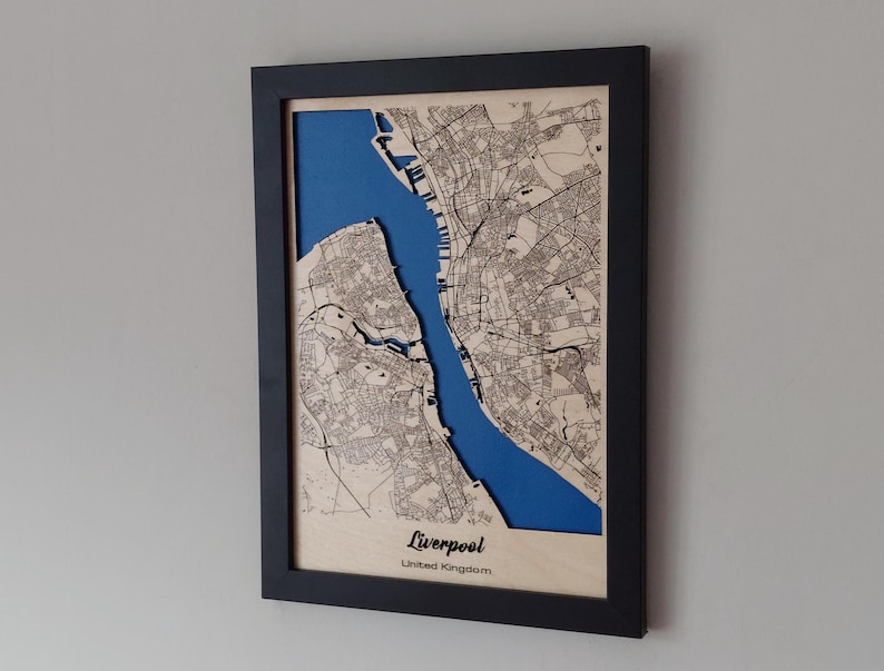 Pu&ograve; includere: Una mappa di legno incorniciata di Liverpool, Regno Unito, con un ritaglio blu del fiume Mersey. La mappa &egrave; tagliata al laser e presenta un design dettagliato della mappa stradale.