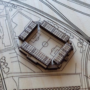 Pu&ograve; includere: Un modello in legno di uno stadio con un design dettagliato, che include un campo e posti a sedere. Il modello &egrave; posizionato su uno sfondo in legno con un design di mappa della citt&agrave;.