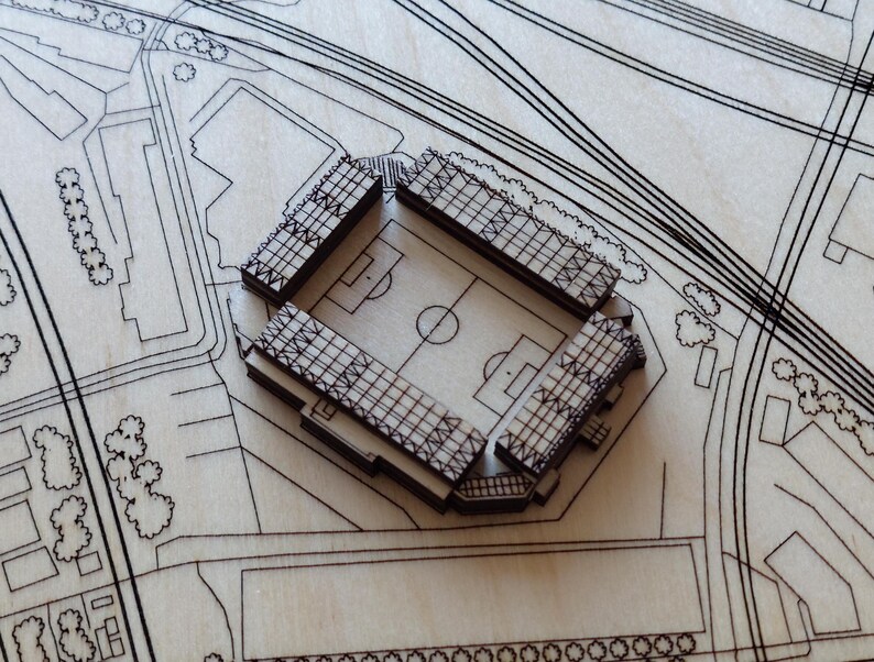Pu&ograve; includere: Un modello in legno di uno stadio con un design dettagliato, che include un campo e posti a sedere. Il modello &egrave; posizionato su uno sfondo in legno con un design di mappa della citt&agrave;.