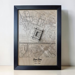 May include: A framed wall art piece featuring a laser-engraved wooden map of the San Siro stadium area in Milan, Italy. The artwork includes a raised, three-dimensional model of the stadium structure and text reading San Siro, Milan, Italy, Since 1926.