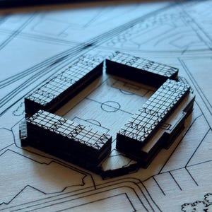 Pu&ograve; includere: Un modello dettagliato di un complesso di edifici, costruito in legno e con un motivo a griglia sull'esterno. Il modello &egrave; posizionato su una superficie simile a un progetto.