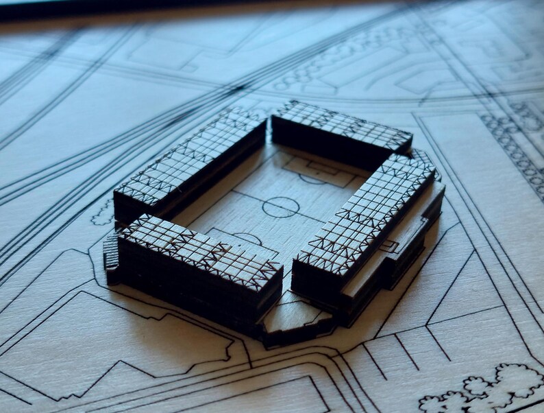 Pu&ograve; includere: Un modello dettagliato di un complesso di edifici, costruito in legno e con un motivo a griglia sull'esterno. Il modello &egrave; posizionato su una superficie simile a un progetto.