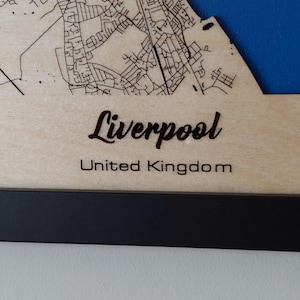 Pu&ograve; includere: Una mappa di legno di Liverpool, Regno Unito, con una cornice nera. La mappa &egrave; tagliata al laser e mostra le strade e i monumenti della citt&agrave;.