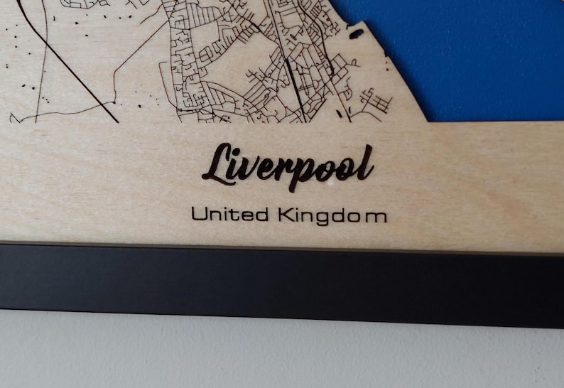 Pu&ograve; includere: Una mappa di legno di Liverpool, Regno Unito, con una cornice nera. La mappa &egrave; tagliata al laser e mostra le strade e i monumenti della citt&agrave;.
