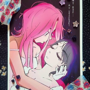 May include: An illustration of two figures with pink and purple hair, embracing. The artwork features the text "MY UNIVERSE!" and "MY GOD..." in vertical text. Decorative crystals and floral accents surround the image.