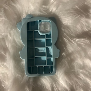 K&ouml;nnte beinhalten: Hellblaue Handyh&uuml;lle in Form einer Cartoonfigur mit Schleife. Die H&uuml;lle hat Aussparungen f&uuml;r Kamera und Kn&ouml;pfe. Sie besteht aus weichem Material und sch&uuml;tzt das Telefon.