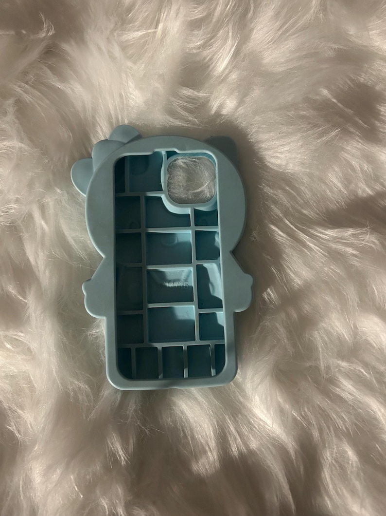 K&ouml;nnte beinhalten: Hellblaue Handyh&uuml;lle in Form einer Cartoonfigur mit Schleife. Die H&uuml;lle hat Aussparungen f&uuml;r Kamera und Kn&ouml;pfe. Sie besteht aus weichem Material und sch&uuml;tzt das Telefon.