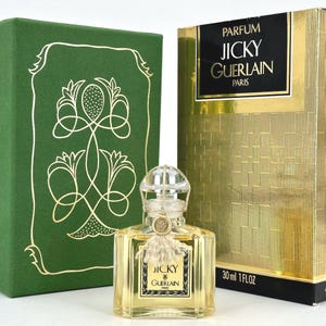 Könnte beinhalten: Ein Vintage-Parfümflakon von Jicky von Guerlain, mit einer transparenten Glasflasche und einem dekorativen, transparenten Verschluss. Die Flasche steht neben einer grünen Schachtel mit goldenen floralen Designs und einer goldenen Schachtel mit dem Parfumnamen. Enthält 30 ml.