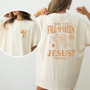 May include: A beige t-shirt with an orange graphic that says "Are you Fall-o-ween Jesus? Matthew 4:19". The graphic includes a cross, flowers, and a pumpkin.