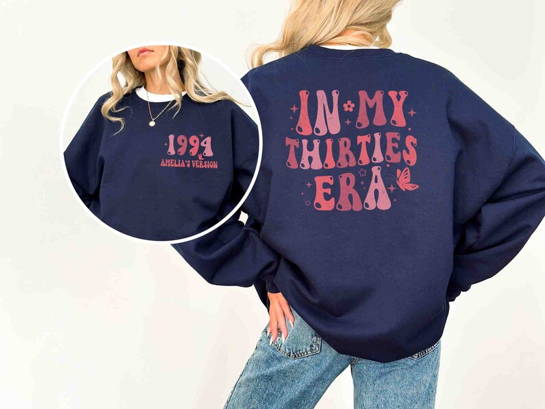 May include: A navy blue sweatshirt with a pink and red graphic on the back that says "In My Thirties Era" with a butterfly and stars. The front of the sweatshirt has a pink and red graphic that says "1994 Amelia's Version".