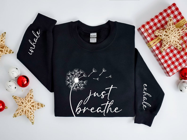 May include: Black sweatshirt with white text that reads "inhale" on the left sleeve, "just breathe" on the front with a dandelion graphic, and "exhale" on the right sleeve.