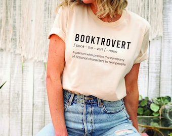 May include: A white t-shirt with black text that reads "BOOKTROVERT [book-tro-vert] . noun A person who prefers the company of fictional characters to real people."