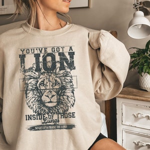 May include: A beige sweatshirt with a lion graphic and the text "You've got a lion inside of those lungs, so get up & praise the Lord."