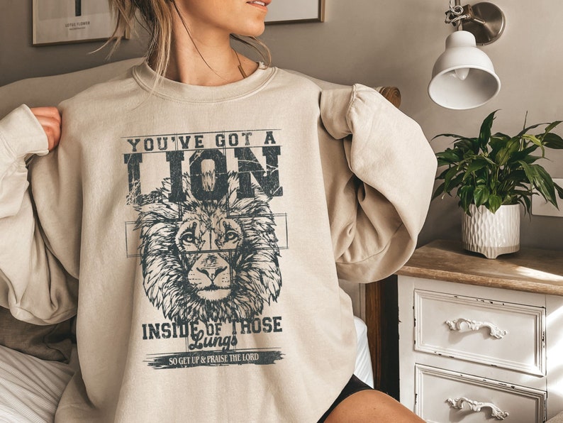 May include: A beige sweatshirt with a lion graphic and the text "You've got a lion inside of those lungs, so get up & praise the Lord."