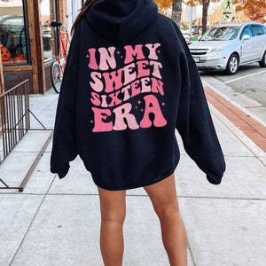 May include: Black hoodie with a pink graphic that says "In My Sweet Sixteen Era" on the back.