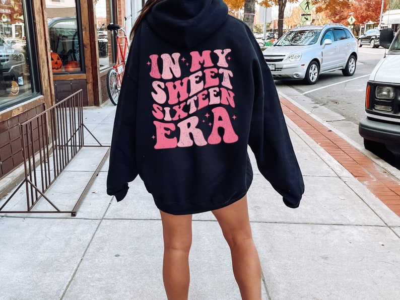 May include: Black hoodie with a pink graphic that says "In My Sweet Sixteen Era" on the back.