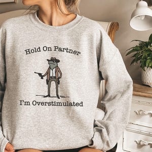 Hold On Partner Im Overstimulated Shirt, Cowboy Frog Sweatshirt, Unhinged Tshirt, Weirdcore Outfits, Gen Z Sweater, Funny Meme Hoodie Tee, Cowgirl Frog Women Sweatshirts, Western Frogs Girl Party Hoodies, Frog Gun Vacation Shirts,Holiday Cowgirls Tee