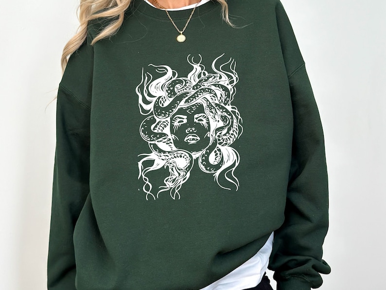 May include: A dark green sweatshirt with a white graphic print of Medusa's head with snakes for hair.