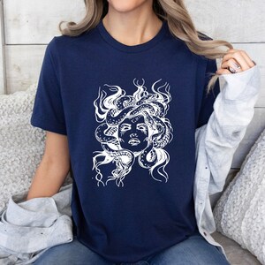 May include: A navy blue t-shirt with a white graphic of Medusa, a mythical Greek figure with snakes for hair.
