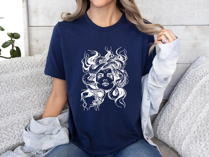May include: A navy blue t-shirt with a white graphic of Medusa, a mythical Greek figure with snakes for hair.