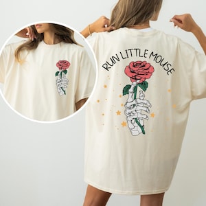 May include: A cream colored t-shirt with a skeleton hand holding a red rose and the text "RUN LITTLE MOUSE" on the back.