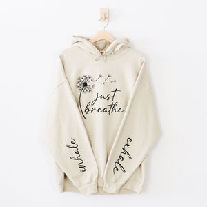 May include: A beige hoodie with a dandelion graphic and the text "just breathe" on the front. The sleeves have the words "inhale" and "exhale" printed on them.