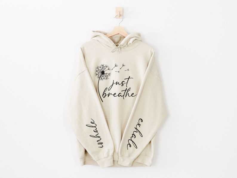 May include: A beige hoodie with a dandelion graphic and the text "just breathe" on the front. The sleeves have the words "inhale" and "exhale" printed on them.