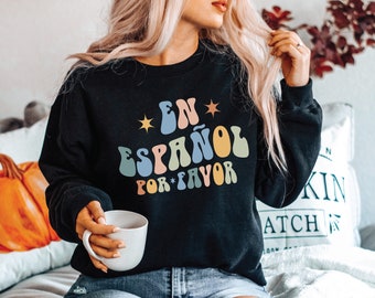 Può includere: Una felpa nera con una grafica retrò colorata che dice "En Español Por Favor" in spagnolo.
