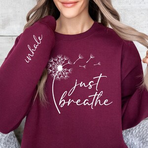 May include: Burgundy sweatshirt with a white dandelion graphic and the text "inhale just breathe".