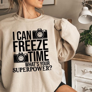 May include: A beige sweatshirt with a black graphic print that says "I can freeze time what's your superpower?" with a camera graphic.